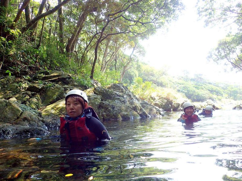 屋久島の沢登りで見られる、木漏れ日が差し込む美しい川の景色と泳ぐ参加者。