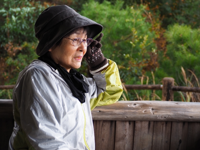 登山ウェアと帽子を身につけ、遠くの景色を穏やかな表情で見つめるシニア女性の横顔。