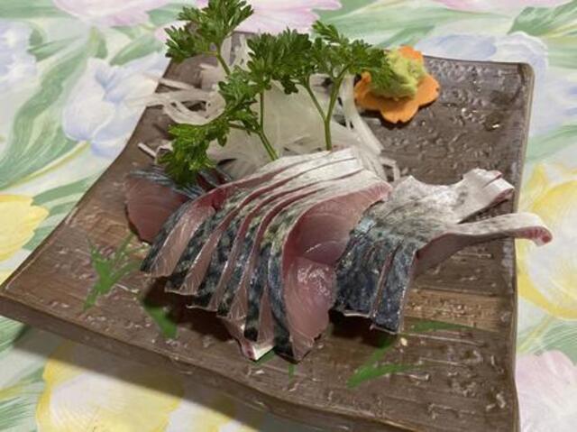 新鮮なサバの刺身が、美しい盛り付けで皿に並べられ、横にわさびと人参の飾りが添えられている