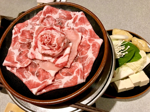 しゃぶしゃぶ用にきれいに並べられた薄切りの豚肉のプレート、豆腐と野菜が添えられている