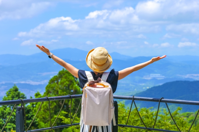 山の展望台から広がる大自然をバックに、両手を広げてポーズを取る女性の写真