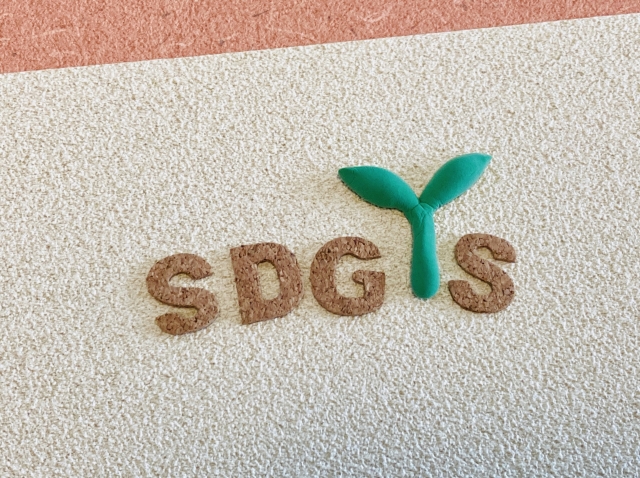 SDGs（持続可能な開発目標）のロゴが、緑色の芽の形で作られたテクスチャーの上に配置されている