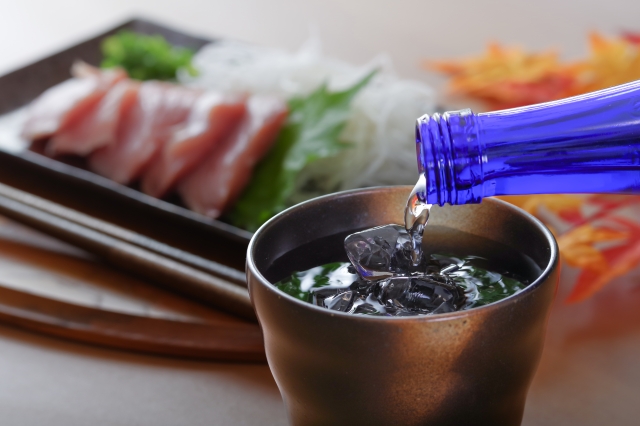 コップに焼酎を注ぐ手元、皿には刺身が並べられている