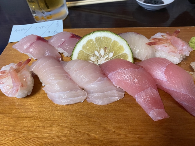 新鮮な寿司が盛り付けられた木の板、レモンのスライスとエビ、さまざまな種類の魚が並んでいる