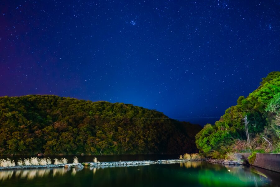 屋久島の山に囲まれた夜の星空と川の風景