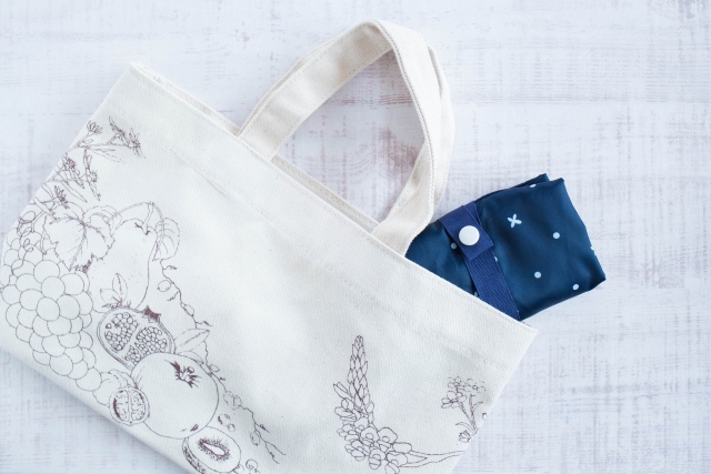 花と果物のデザインが施されたベージュのバッグと折りたたまれたネイビーのエコバッグ