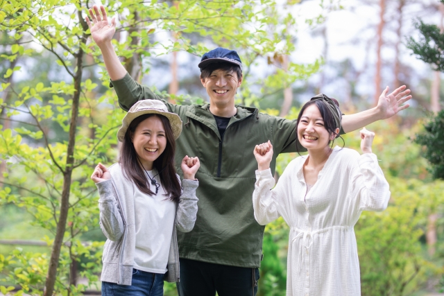 緑の中で元気にポーズを取る3人の若者たちが写った写真