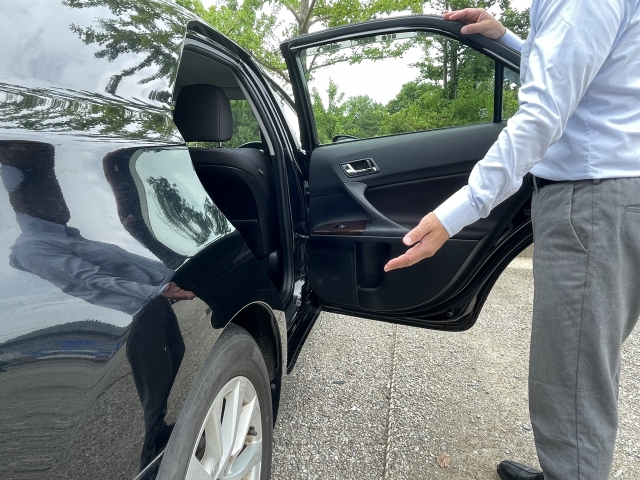 ドアを開けて出迎えるドライバーと黒い送迎車