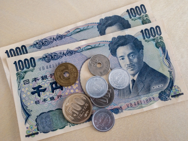 一疊排列整齊的日本日圓鈔票,其中包含千円紙鈔與零錢