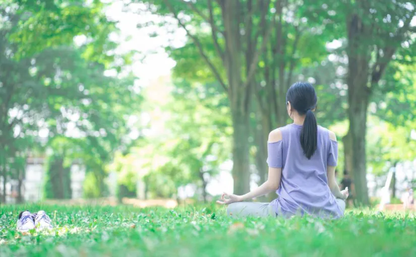 木漏れ日が差す緑の中でヨガをする女性の後ろ姿