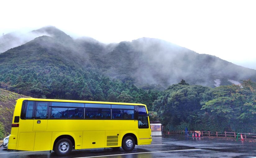 霧に包まれた屋久島の山道を走る黄色い観光バス