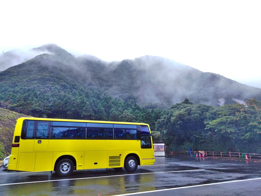 霧に包まれた屋久島の山道を走る黄色い観光バス